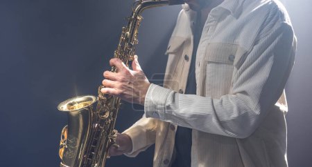 Téléchargez les photos : Saxophone dans les mains d'un homme sur un fond sombre, espace de copie. - en image libre de droit