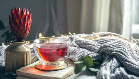 Foto de Una composición acogedora con té rojo, una flor y un elemento de punto sobre un fondo borroso, espacio para copiar. - Imagen libre de derechos