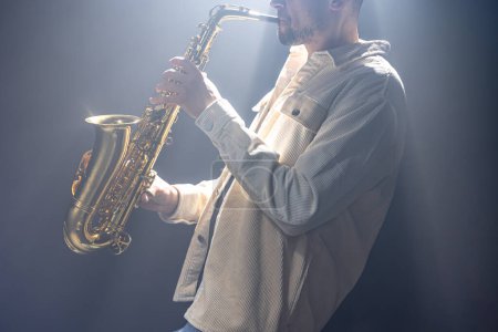 Téléchargez les photos : Musicien masculin sur scène joue le saxophone sombre avec de la fumée. - en image libre de droit