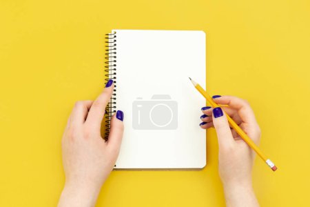 Photo for Blank notepad in female hands on a yellow background, flat lay, concept of hobies, work and creativity, copy space. - Royalty Free Image