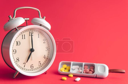 Téléchargez les photos : Time for health check concept. White alarm clock with pills, against the backdrop of Viva Magenta, copy space. - en image libre de droit