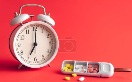 Téléchargez les photos : Time for health check concept. White alarm clock with pills, against the backdrop of Viva Magenta, copy space. - en image libre de droit