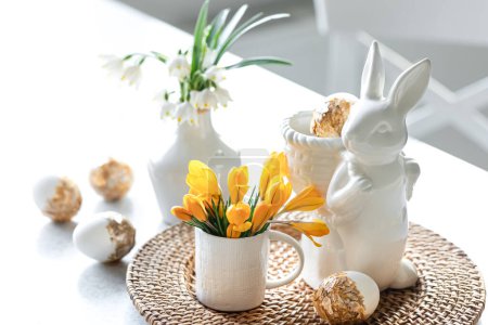 Osterstillleben mit Keramikhasen, Ziereiern und ersten Frühlingsblumen.