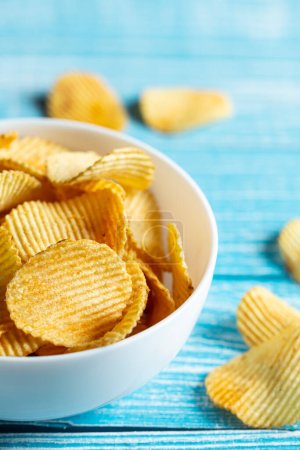 Photo for Close-up, a plate of potato chips on a blurred blue wooden background. - Royalty Free Image