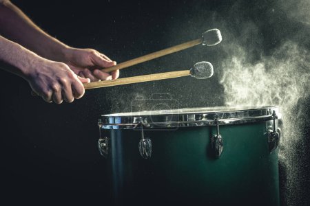 Photo for The percussionist plays with sticks on the floor tom on under studio lighting.. Concert and performance concept. - Royalty Free Image
