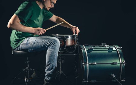 Foto de Un baterista masculino y un kit de batería sobre un fondo negro, el músico se prepara para tocar, copiar espacio. - Imagen libre de derechos