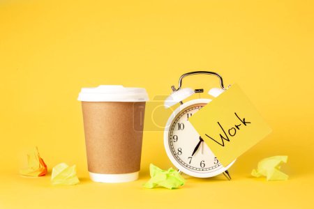 Paper cup and alarm clock with paper reminder with the inscription Work on a yellow background isolated.