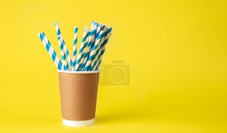 Téléchargez les photos : Coupe en papier jetable avec des pailles en papier rayé pour les boissons sur un fond jaune isolé. - en image libre de droit