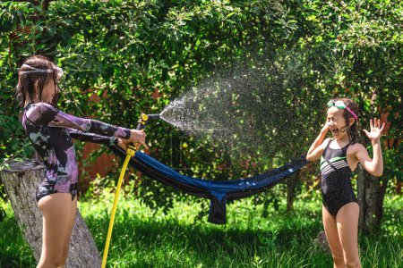 Téléchargez les photos : Adorables petites filles jouant avec un tuyau d'arrosage lors d'une chaude journée d'été. Enfants s'amusant avec de l'eau, activités d'été en plein air pour les enfants. - en image libre de droit