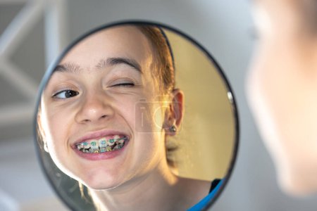 Chica preadolescente caucásica con frenos en los dientes mirando al espejo, concepto de sonrisa perfecta.