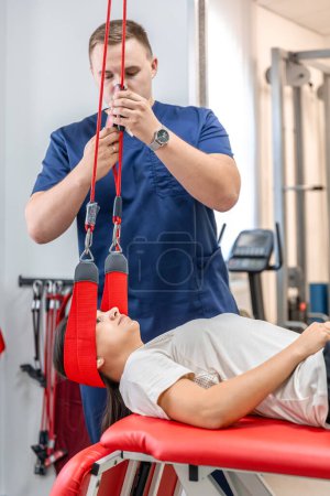Photo for Female patient hanging on suspensions at rehabilitation center. Therapeutic exercises and neuromuscular activation on red cord slings, Neurac technique. - Royalty Free Image
