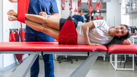 Paciente femenina suspendida en suspensión en centro de rehabilitación, ejercicios terapéuticos y activación neuromuscular en eslingas de cuerda roja, técnica Neurac.