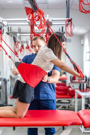 Photo for Rehabilitation specialist doing active treatment on suspension straps to female patient. Concept of therapeutic exercises to restore pain-free movement patterns and improve function, Neurac technique. - Royalty Free Image