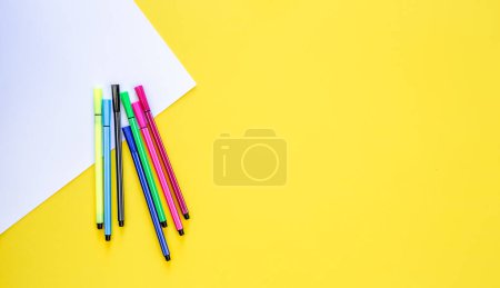 Téléchargez les photos : Un ensemble de feutres et une feuille de papier blanc sur fond jaune, vue du dessus, espace de copie. - en image libre de droit