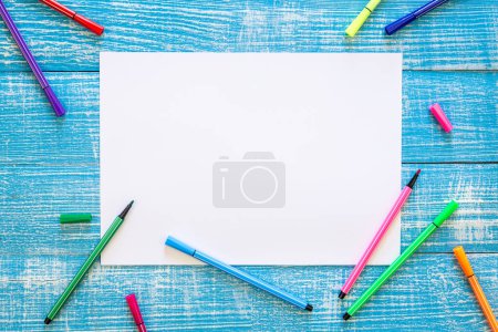 Téléchargez les photos : Un ensemble de stylos à pointe de feutre et une feuille de papier blanc vierge sur un fond en bois bleu, vue du dessus, espace de copie. - en image libre de droit