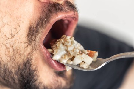 Photo for A hungry man opened his mouth, ready to eat a spoonful of porridge with fruit, close-up. - Royalty Free Image