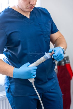 Foto de Dispositivo de terapia de ondas de choque con manos de médico masculino en guantes de goma, el campo magnético, rehabilitación. - Imagen libre de derechos