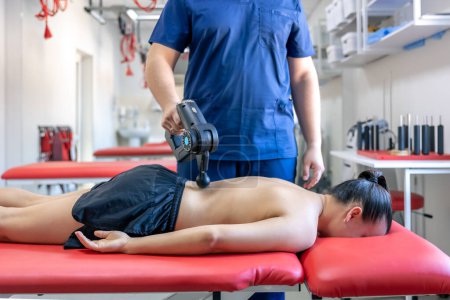 Téléchargez les photos : Médecin massant le dos d'une patiente avec un pistolet masseur à percussion. - en image libre de droit
