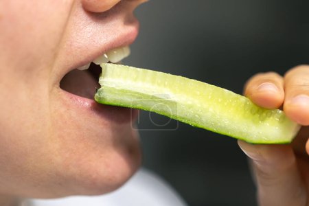 Téléchargez les photos : Plan détaillé d'une femme mange un morceau de concombre frais, gros plan. - en image libre de droit