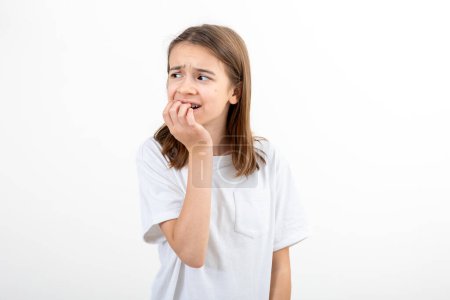 Photo for Portrait of a scared, afraid and anxious little girl in white t-shirt, biting her fingernails, human emotions concept, copy space. - Royalty Free Image
