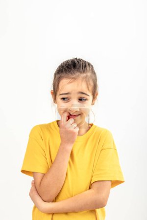 Photo for Portrait of a scared, afraid and anxious little girl in yellow t-shirt on a white background isolated, biting her fingernails, human emotions concept. - Royalty Free Image
