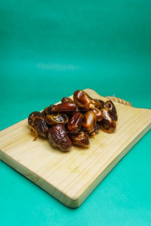 A pile of dates or phoenix dactylifera which is usually consumed by Muslims when breaking the fast in the month of Ramadan. Isolated on green background.