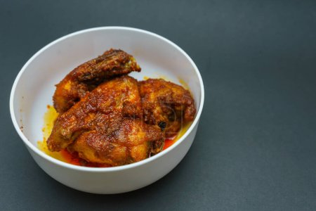 Homemade ayam sambal balado or spicy fried chicken is Traditional food from Padang, West Sumatra. Served on bowl and isolated on black background.