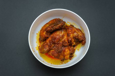 Homemade ayam sambal balado or spicy fried chicken is Traditional food from Padang, West Sumatra. Served on bowl and isolated on black background.