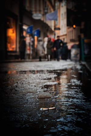 A shallow puddle on a cobblestone street reflects a muted city life on a rainy day.