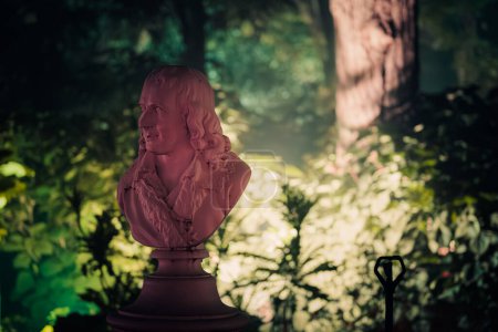 Eine sanft beleuchtete Büste Voltaires in einem Garten, die historische und philosophische Betrachtung ausstrahlt.