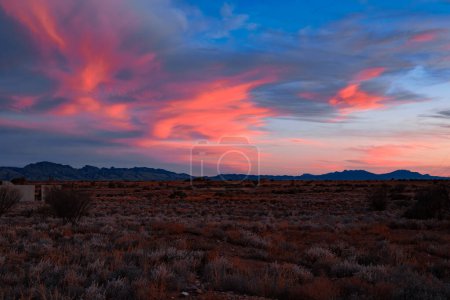 Leuchtend rote Wolken schmücken den Abendhimmel über einer heiteren Wüstenlandschaft.