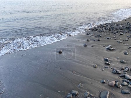 Ola de agua en la playa con arena gris y piedras corales rocas