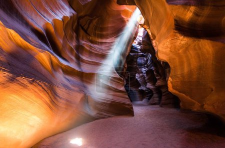 A beam of light shines through a slender opening in the rock formation of a canyon, illuminating the surroundings with a striking contrast.