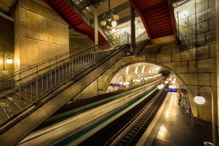 A train in Paris is captured in motion as it passes through a tunnel located alongside a platform.