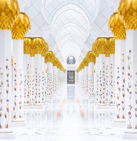 Symmetrische Ansicht der Scheich-Zayed-Moschee-Arkaden in Abu Dhabi. Goldene Palmsäulen säumen den Weg, der zu einem kunstvollen Eingang innerhalb der Sheikh Zayed Moschee führt.