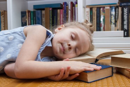 Foto de Niña linda durmiendo con libros en la parte delantera de la estantería. Concepto de educación, fondo de enfoque suave - Imagen libre de derechos