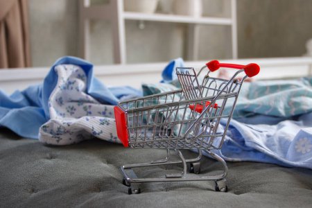Photo for Empty shopping cart and different clothes on the bad. Concept of purchases or shopping - Royalty Free Image
