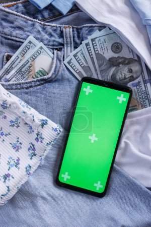 Foto de Pantalones vaqueros azules con dólares americanos en el bolsillo, y un teléfono inteligente con pantalla verde, vista superior. Concepto de viajar o ir de compras - Imagen libre de derechos