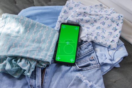 Téléchargez les photos : Différents vêtements et un smartphone avec écran vert, vue sur le dessus. Concept de voyage ou d'achat en ligne - en image libre de droit