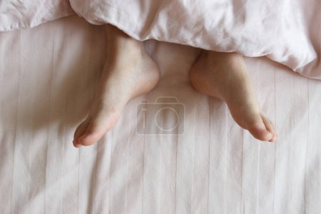 Téléchargez les photos : Pieds sous une couverture légère sur le lit. Concept de dormir ou de se réveiller le matin - en image libre de droit