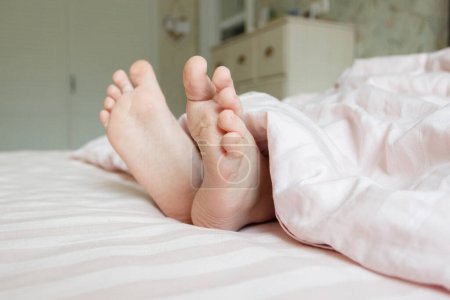 Téléchargez les photos : Pieds sous une couverture légère sur le lit. Concept de dormir ou de se réveiller le matin - en image libre de droit