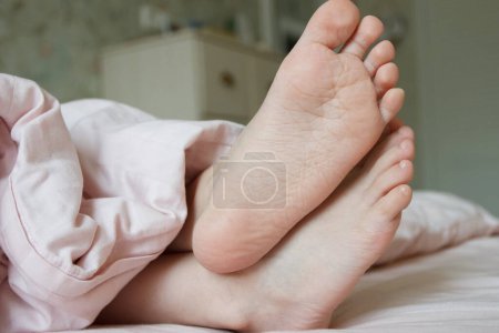 Photo for Feet under a light blanket on the bed. Concept of sleeping or waking in the morning - Royalty Free Image