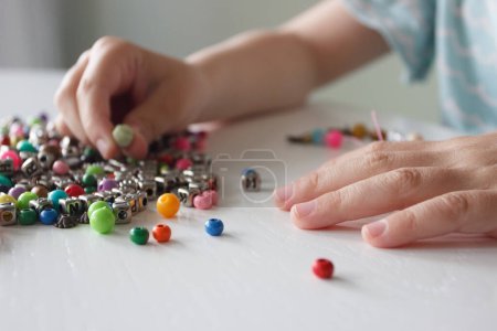 Téléchargez les photos : Processus de fabrication d'un bracelet à partir d'un fil et de perles de couleur, concept de passe-temps ou de loisirs - en image libre de droit