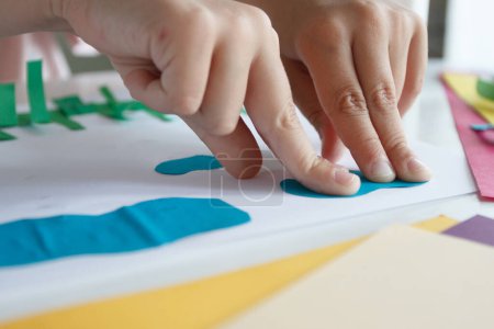 Téléchargez les photos : Enfant mignon créant une application avec du papier coloré et de la colle. Concept de passe-temps et d'éducation - en image libre de droit