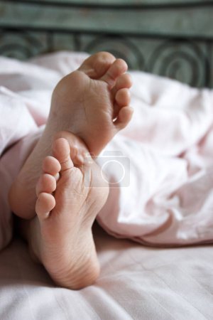 Photo for Feet under a light blanket on the bed. Concept of sleeping or waking in the morning - Royalty Free Image