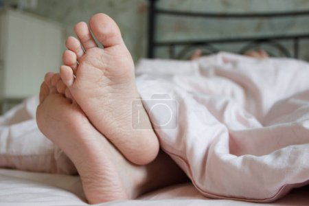 Foto de Pies debajo de una manta ligera en la cama. Concepto de dormir o despertarse por la mañana - Imagen libre de derechos