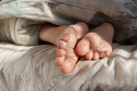 Füße unter einer hellen Decke auf dem Bett. Konzept des gesunden Lebens