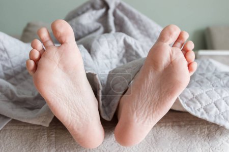 Foto de Pies debajo de una manta ligera en la cama, fondo de enfoque suave. Concepto de salud - Imagen libre de derechos
