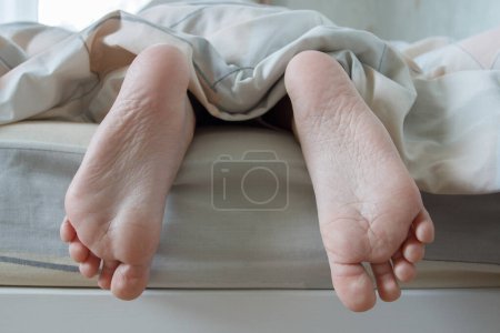 Photo for Feet under a light blanket on the bed, soft focus background. Concept of health - Royalty Free Image