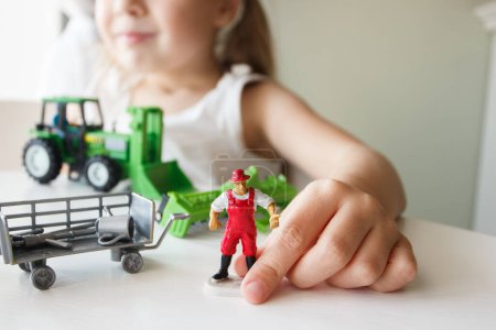 Photo for Cute child plays with farm equipment toys. Business or farming concept, blurred background - Royalty Free Image